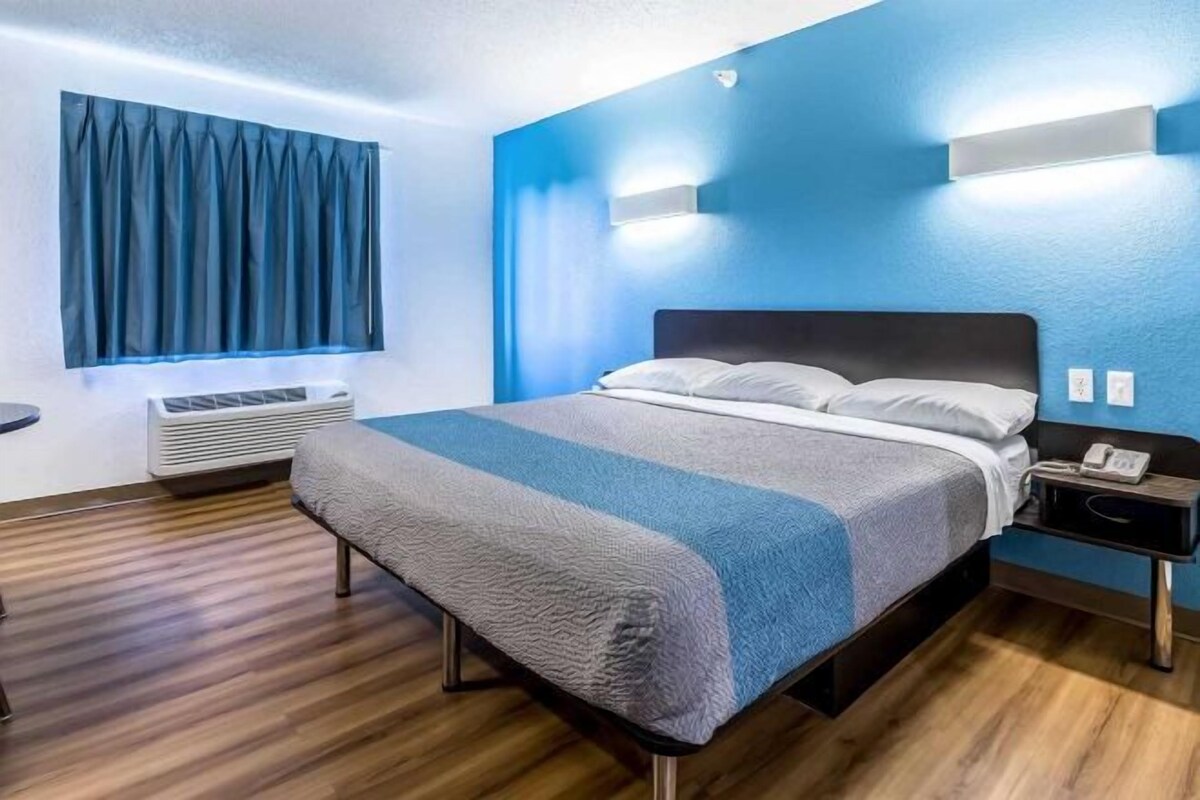 Een hotelkamer met een bed, nachtkastje en een raam met gordijnen.