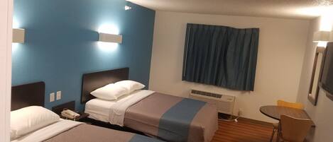 Camera d'albergo con due letti, una scrivania, una sedia, una TV e una finestra con tende.