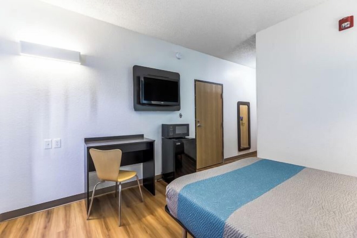 Een hotelkamer met een bed, een bureau met stoel, een televisie en een deur.