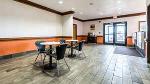A clean, well-lit indoor area with a reception desk, a seating area with tables and chairs, and a view through the glass doors.
