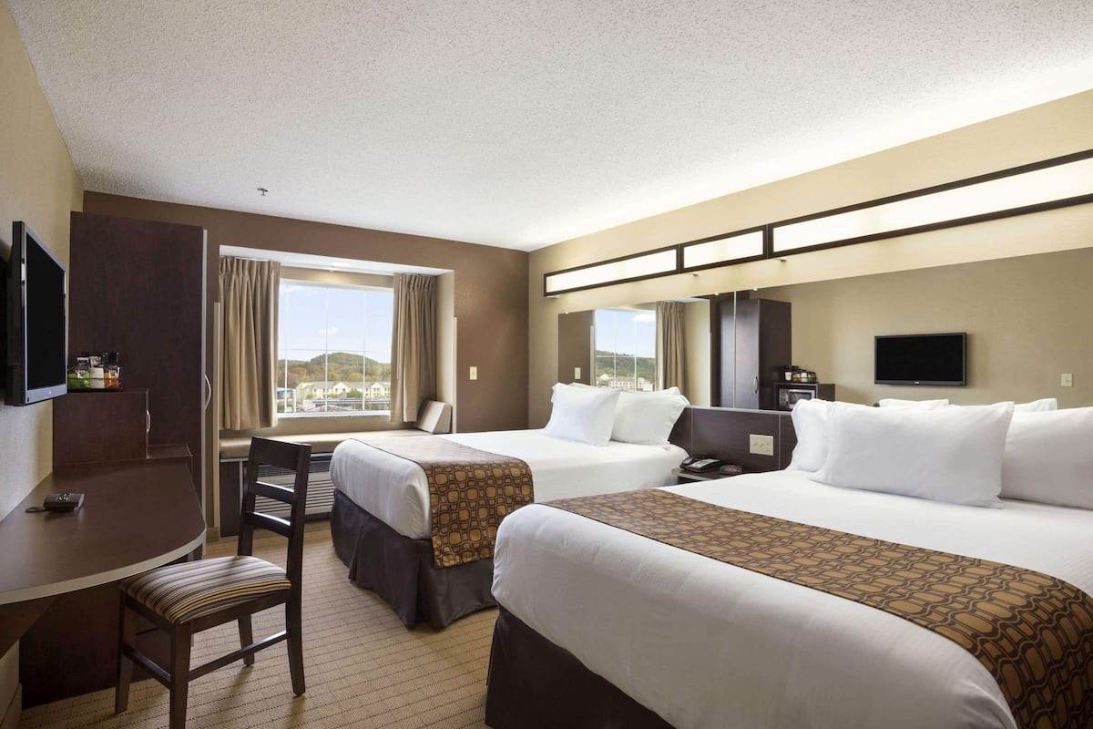 A hotel room with two beds, a desk, a chair, and a TV.
