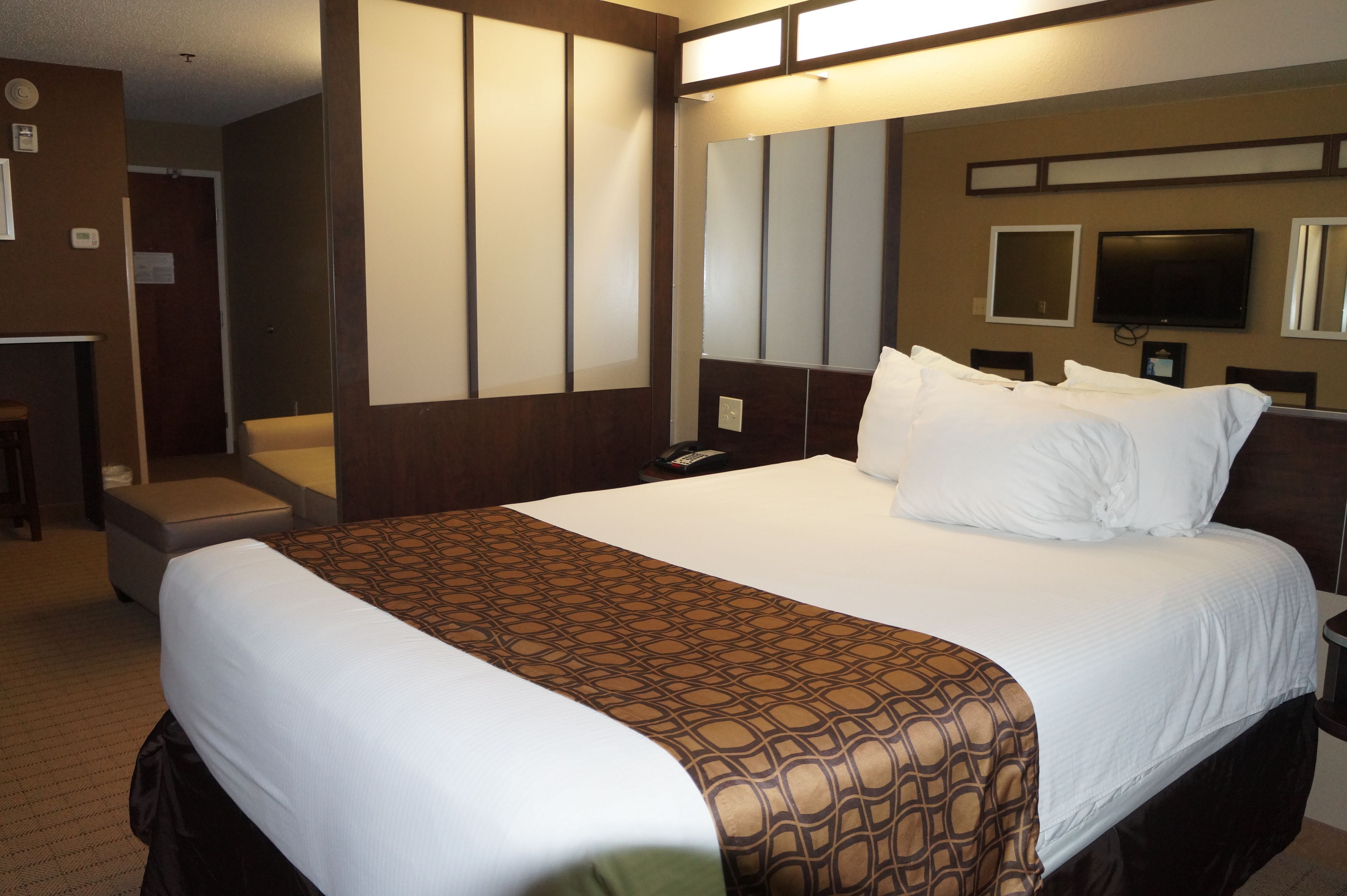 Ein Hotelzimmer mit einem großen Bett, einem Nachttisch, einem Fernseher und einem Spiegel an der Wand.