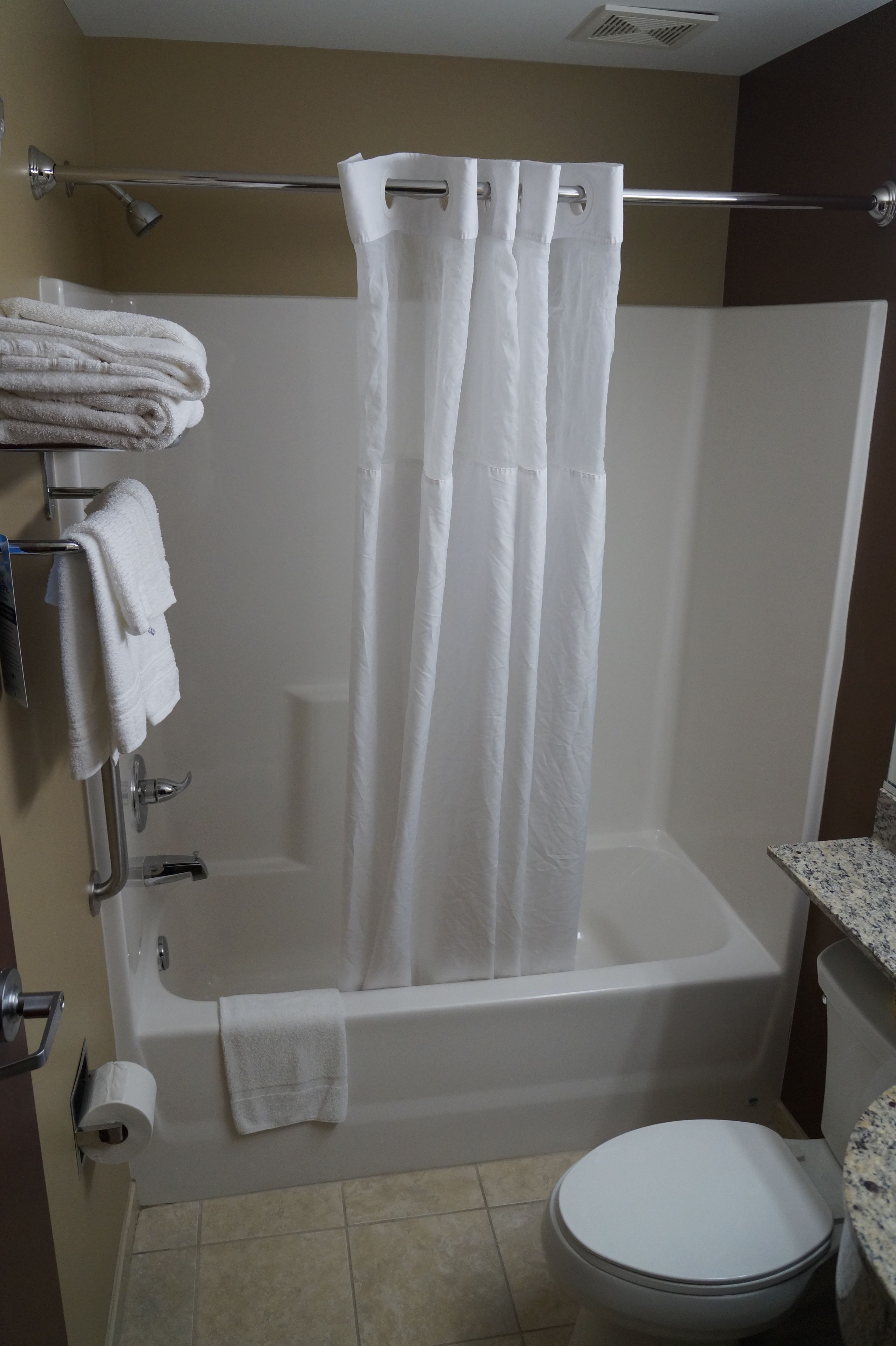 Baño con bañera, inodoro y toallero con toallas dobladas.