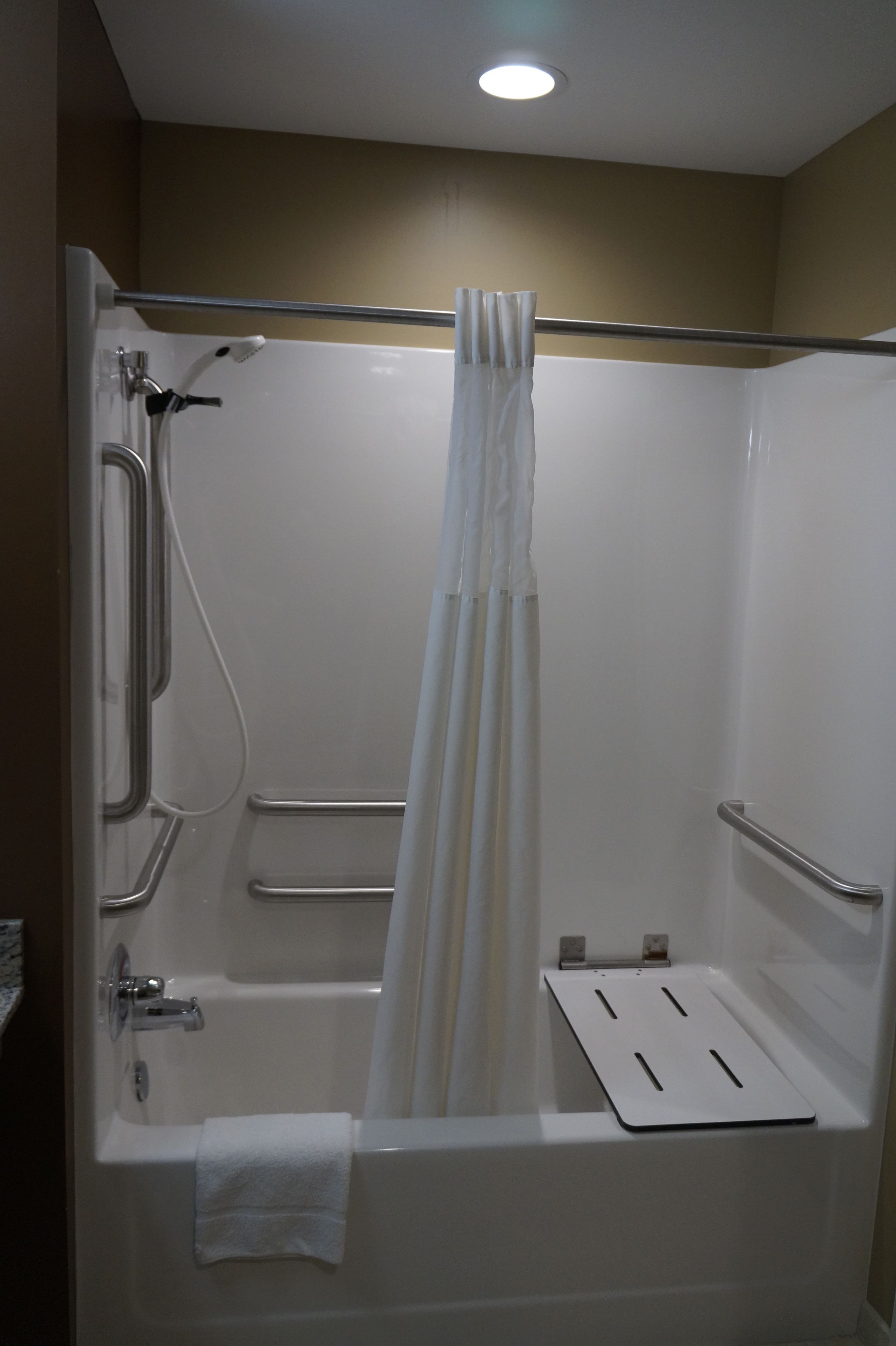 Una bañera blanca con cortina de ducha, barras de apoyo y un perchero para toallas.