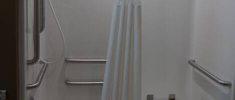 Una bañera blanca con cortina de ducha, barras de apoyo y un perchero para toallas.