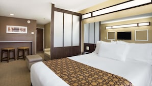 A hotel room with a large bed, a desk with two stools, a flat-screen TV, and a minibar. - Microtel Inn & Suites by Wyndham Cambridge (Cambridge)