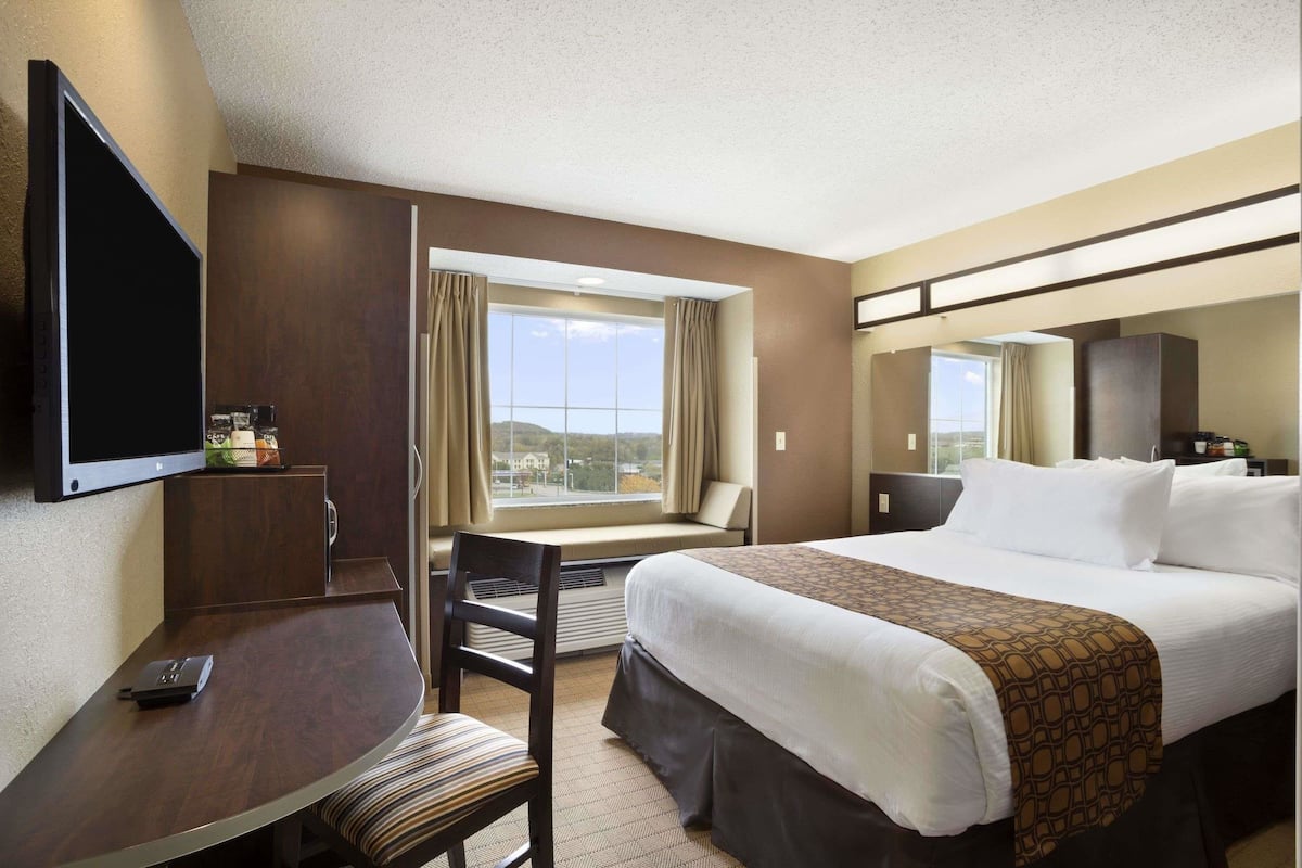 A hotel room with a large bed, a desk with a chair, a television, and a window with curtains.