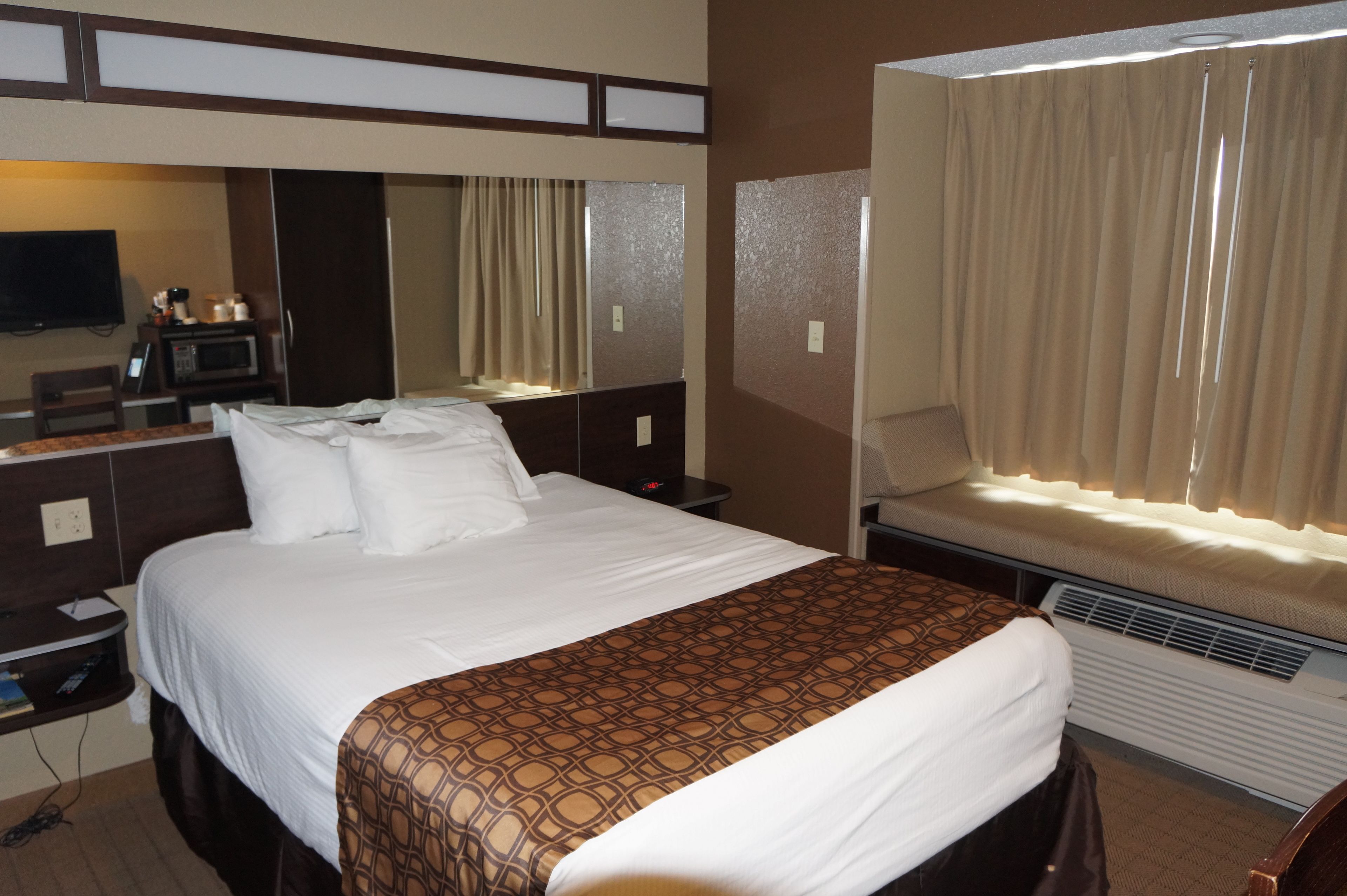 Habitación de hotel con una cama grande, una mesita de noche con lámpara, televisión y ventana con cortinas.
