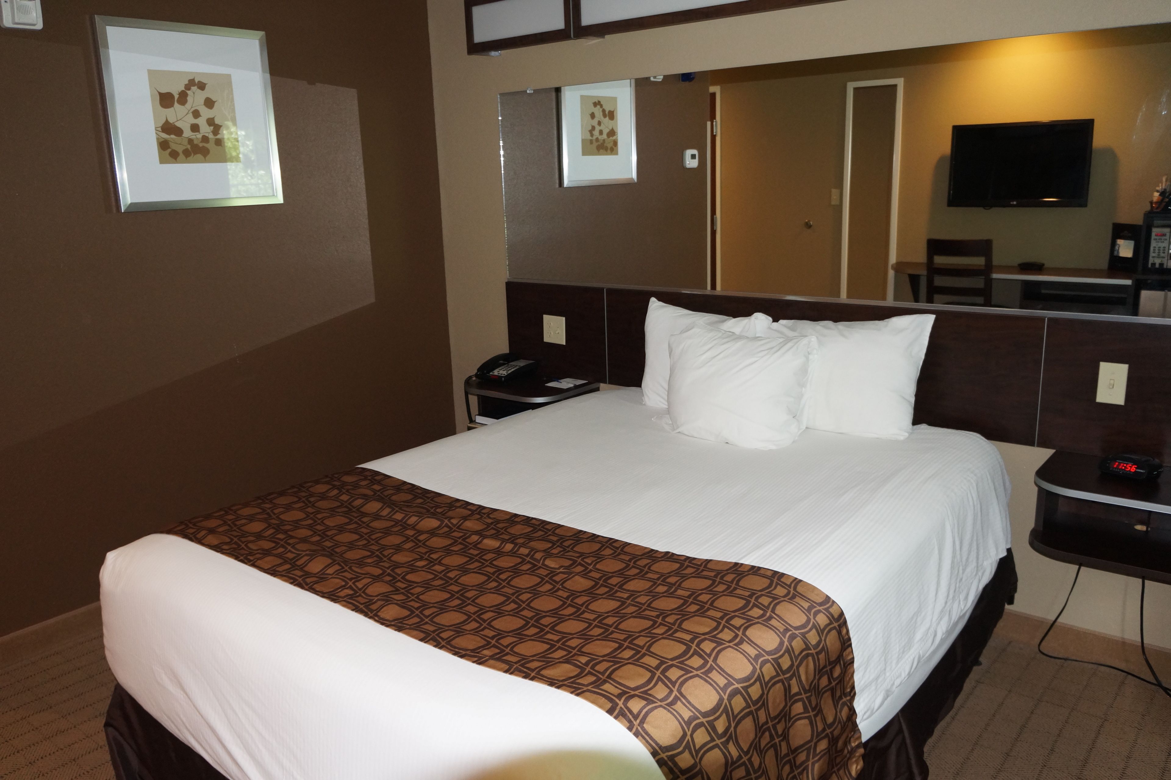 A hotel room with a large bed, a bedside table with a phone, a nightstand with a clock, and a TV on the wall.