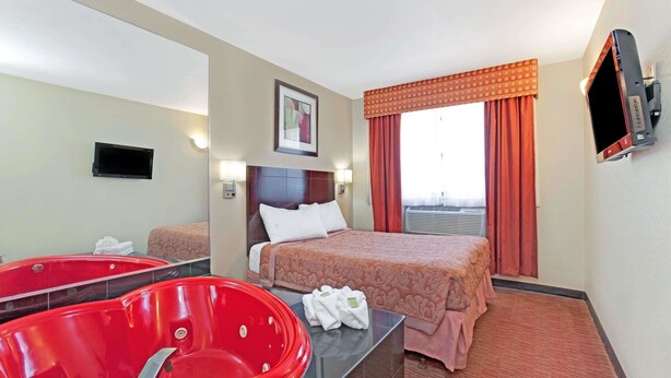 A hotel room with a bed, a red bathtub, a television, and a window with curtains. - Super 8 by Wyndham Long Island City LGA Hotel (Astoria)