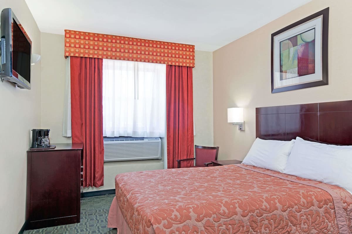 Ein Hotelzimmer mit Bett, Schreibtisch, Stuhl, Fernseher und einem Fenster mit roten Vorhängen.