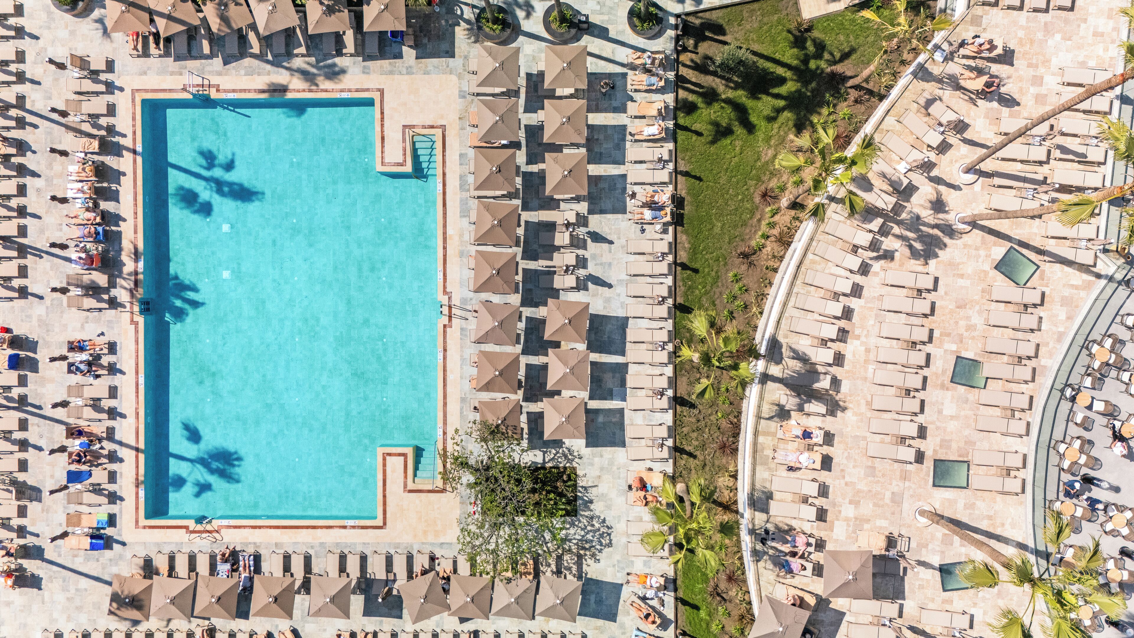 Ein Luftbild eines Hotels mit Schwimmbad, Liegestühlen und Außenbereich mit Sitzgelegenheiten.