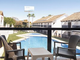 A hotel balcony with a pool, lounge chairs, and a view of the hotel buildings.