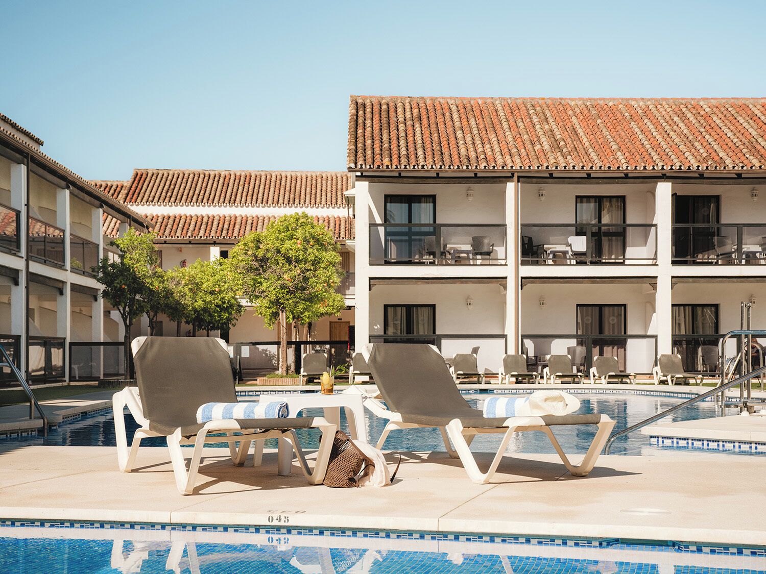 Una piscina al aire libre, sombrillas, sillones reclinables de piscina