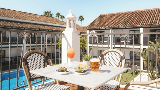 A table with a drink, a pitcher, and bowls of food, overlooking a swimming pool with a building in the background. - Hotel Ona Diana Park (Estepona)