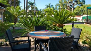 An outdoor dining area with a round table and four chairs, surrounded by lush greenery and palm trees.