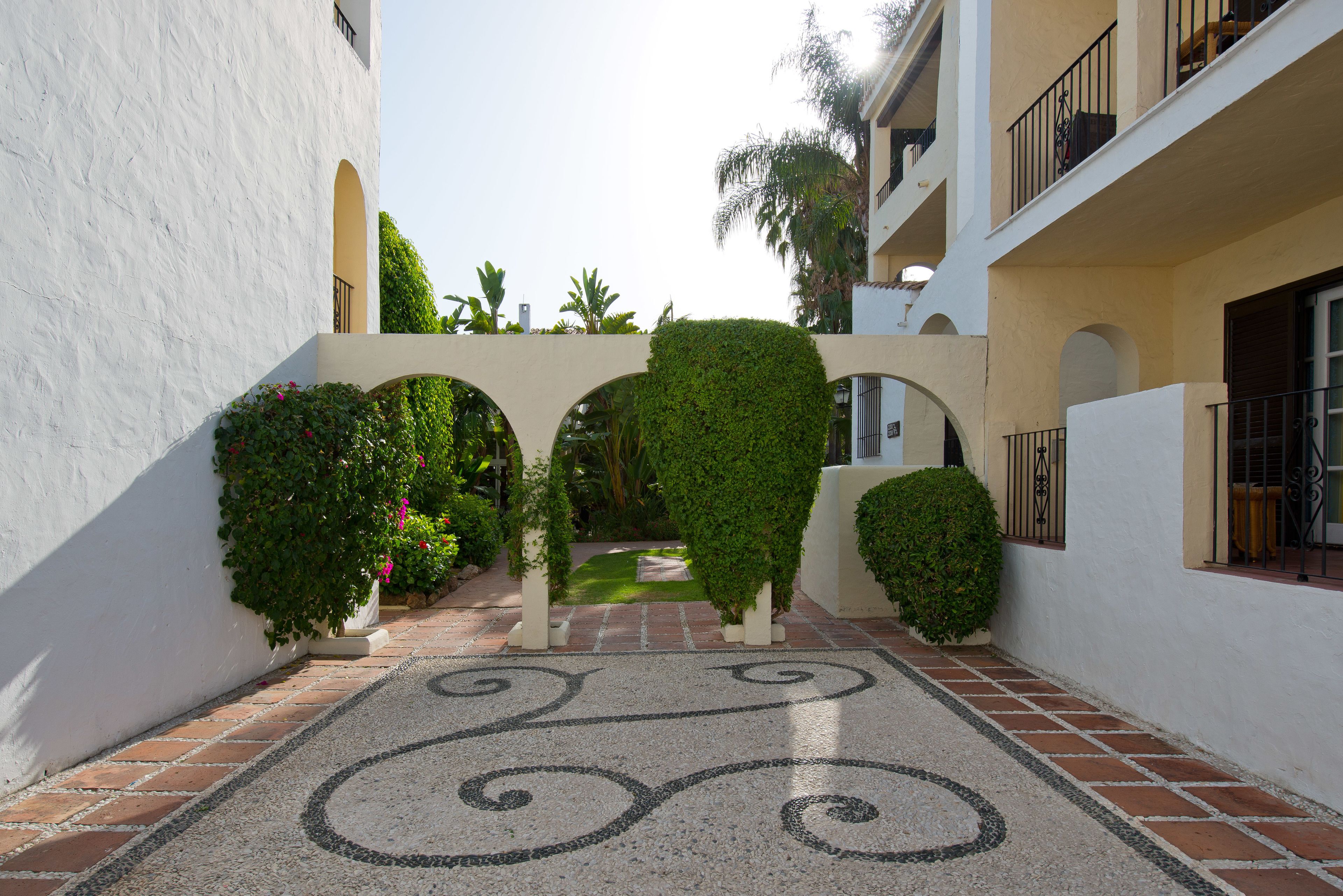A courtyard with a tiled floor, an archway, and greenery.