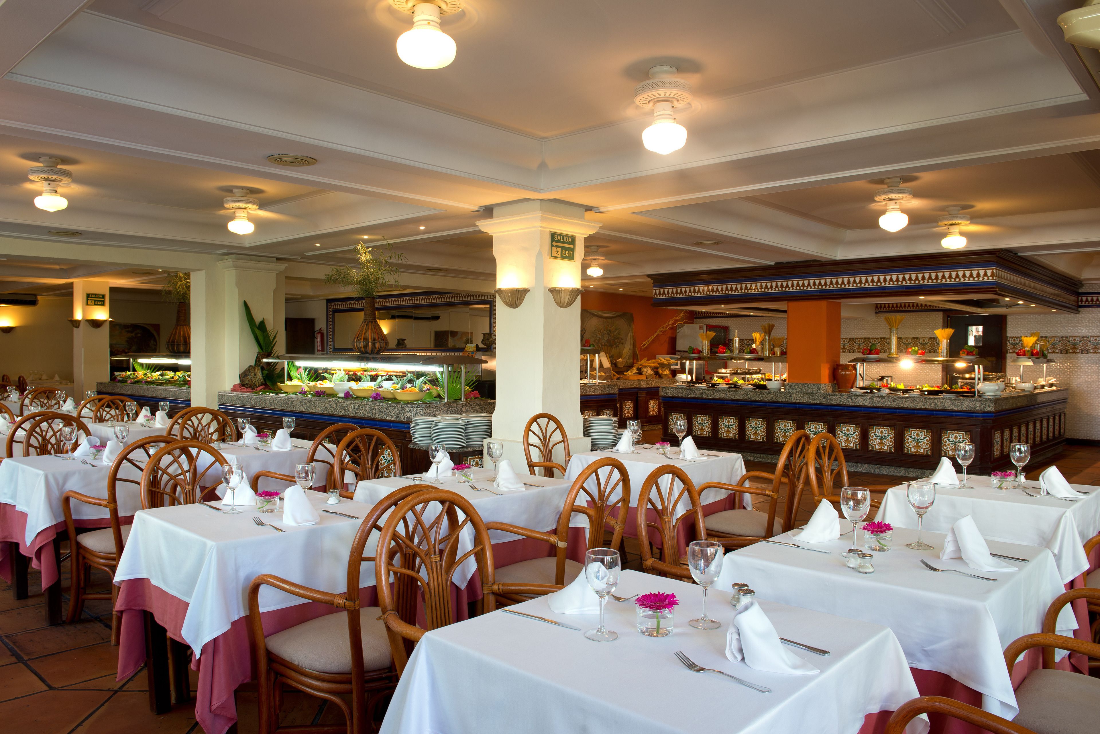 Ein Restaurant mit mehreren Tischen, gedeckt zum Essen, mit weißen Tischdecken und Holzstühlen.