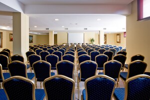 Une salle de conférence avec des rangées de chaises bleues et un tableau blanc à l’avant.