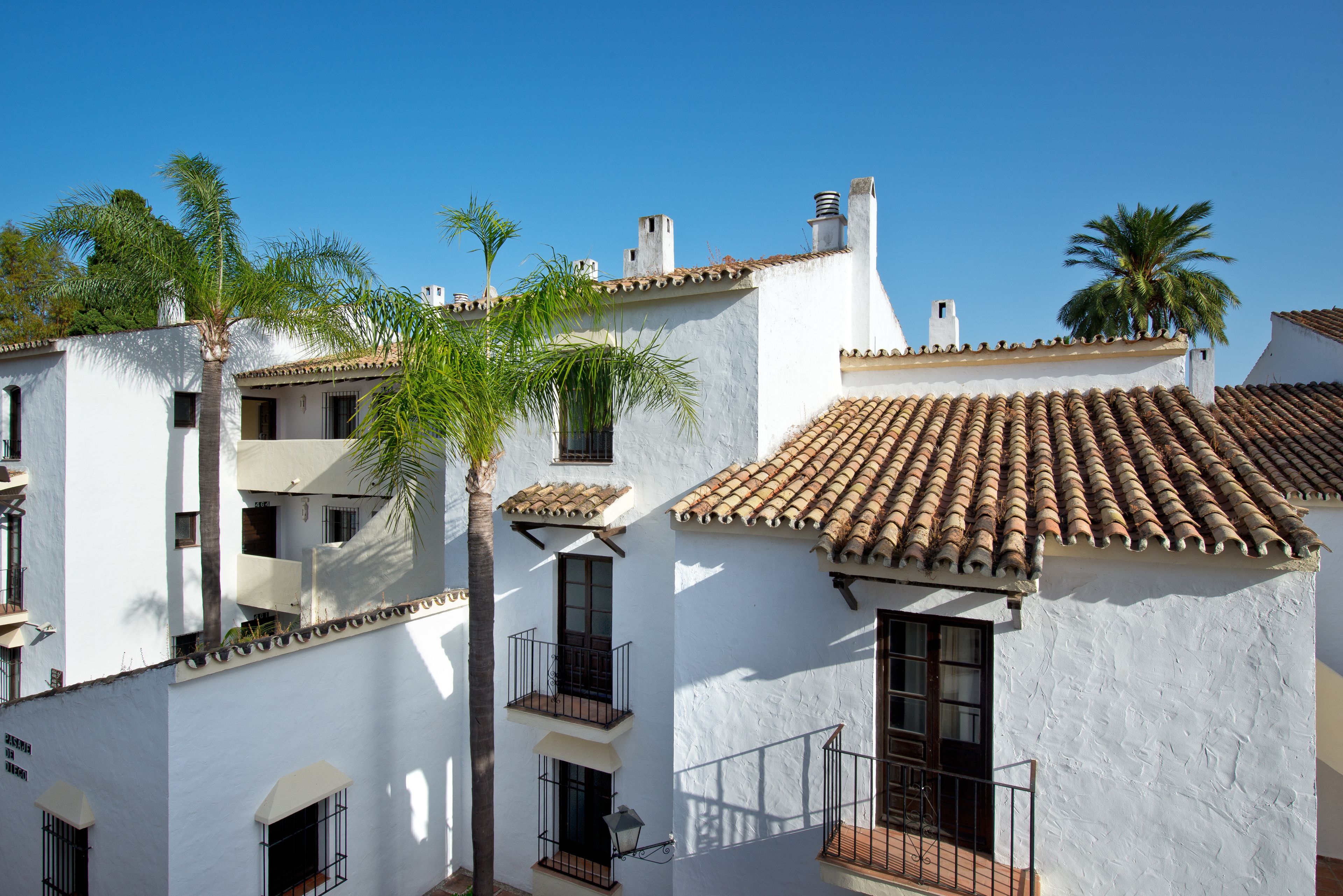 Un edificio blanco con tejas de terracota, balcones y palmeras.