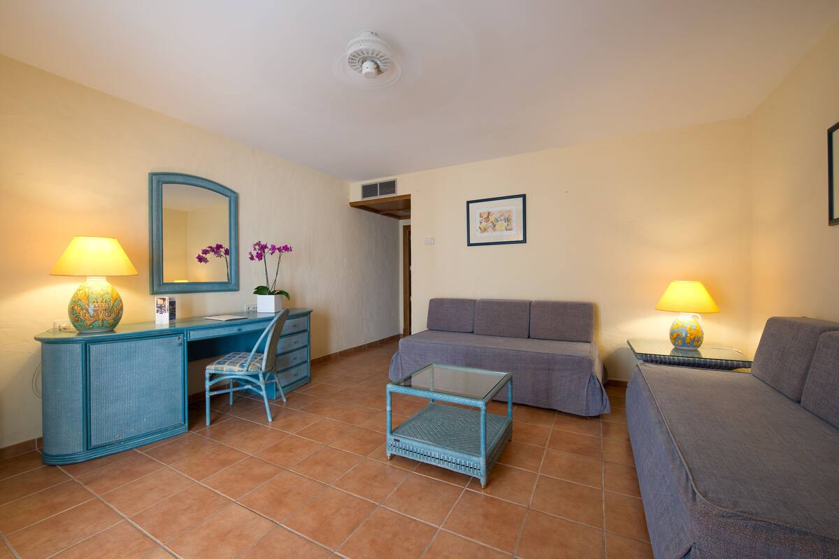 Een compacte woonkamer met een blauw bureau, een stoel, een bank en een klein bijzettafeltje.