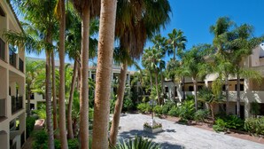 A courtyard with palm trees, a central planter with flowers, and a building with balconies. - Hotel BlueBay Banús (Marbella)