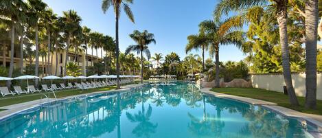Una piscina rodeada de palmeras y sillas de descanso.