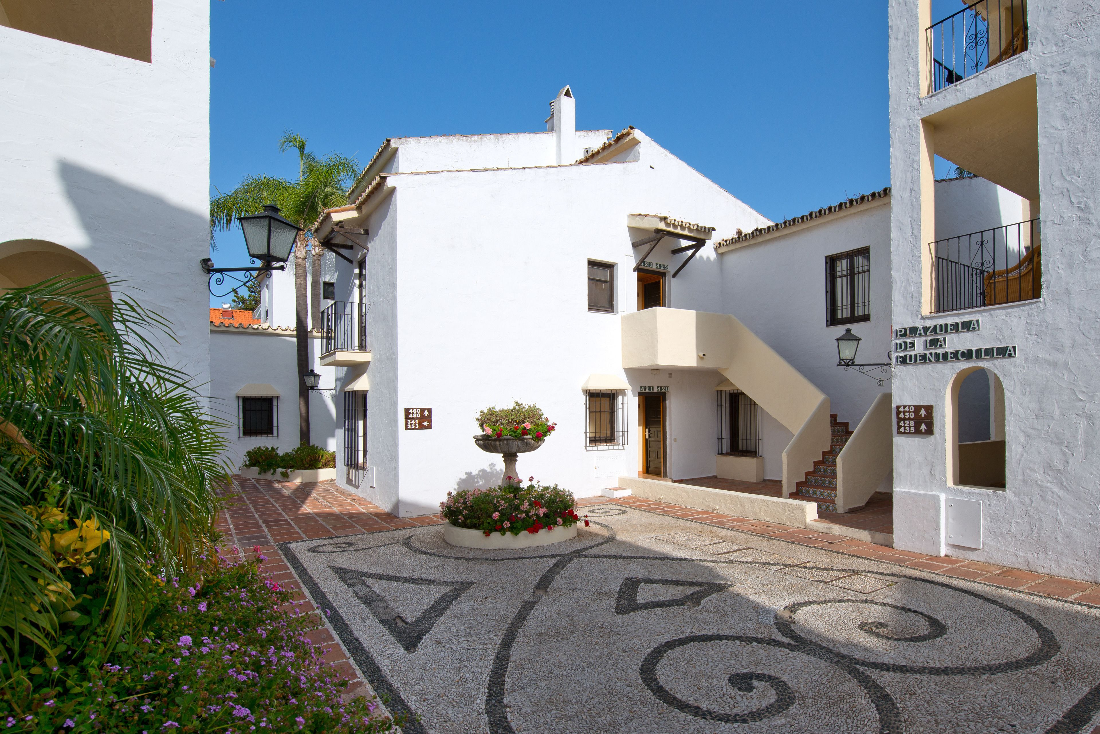 A courtyard with white buildings, a fountain, and a sign indicating 'Plaza de la Fuentecilla'.