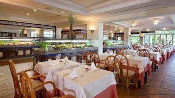 A restaurant with multiple tables, each set with white tablecloths and wooden chairs.