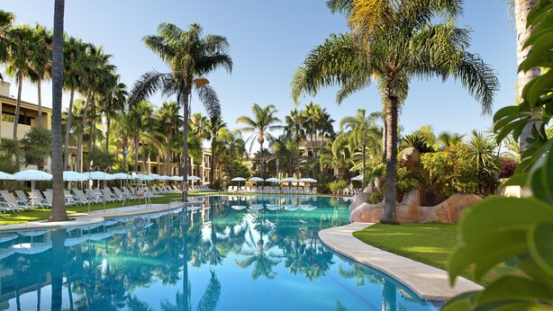 A pool surrounded by palm trees and lounge chairs. - Hotel BlueBay Banús (Marbella)