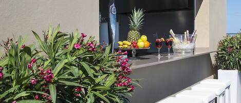 An outdoor bar area with a modern design, featuring a grill, seating, and a variety of fruits and drinks.