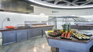 Un bufé con diversas frutas y bebidas, un expositor de vidrio y un diseño moderno de techo.