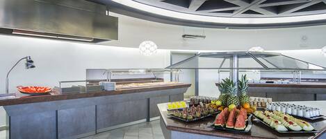 A buffet with various fruits and beverages, a glass display case, and a modern ceiling design.