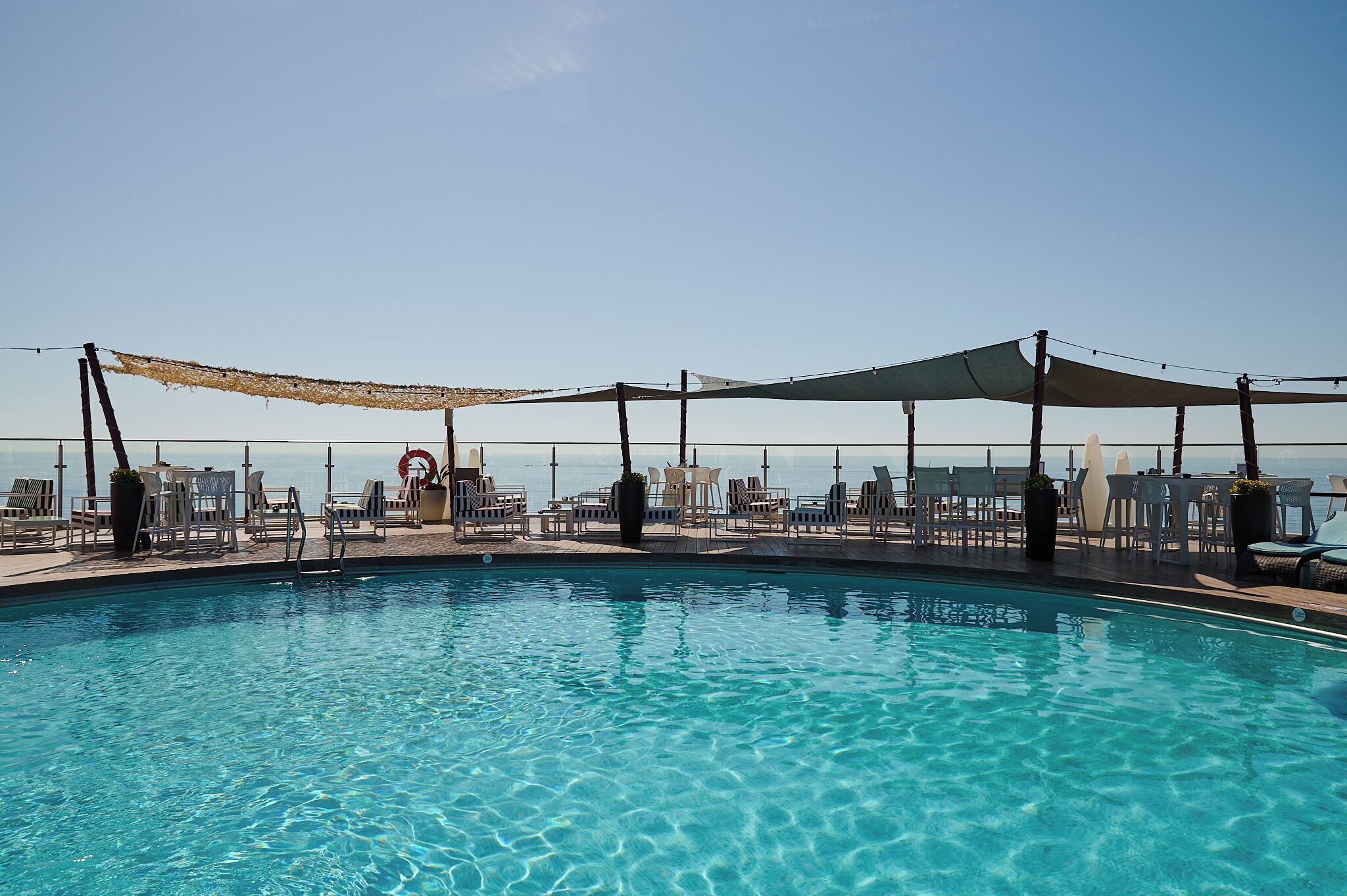A pool area with clear blue water, surrounded by lounge chairs and umbrellas, overlooking a body of water.