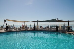 A pool area with clear blue water, surrounded by lounge chairs and umbrellas, overlooking a body of water.