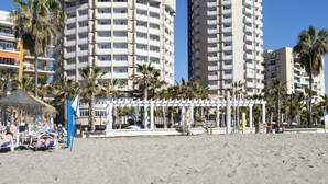 A beachside hotel with a circular building, palm trees, and a beach area with umbrellas. - Hotel El Puerto by Pierre & Vacances (Fuengirola)