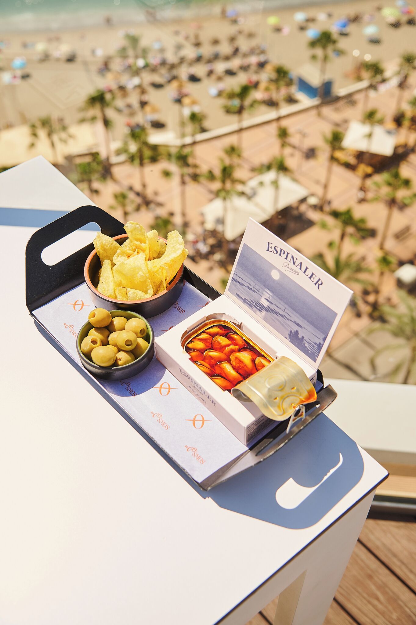 Una bandeja con aperitivos y un menú en un balcón con vista al mar.