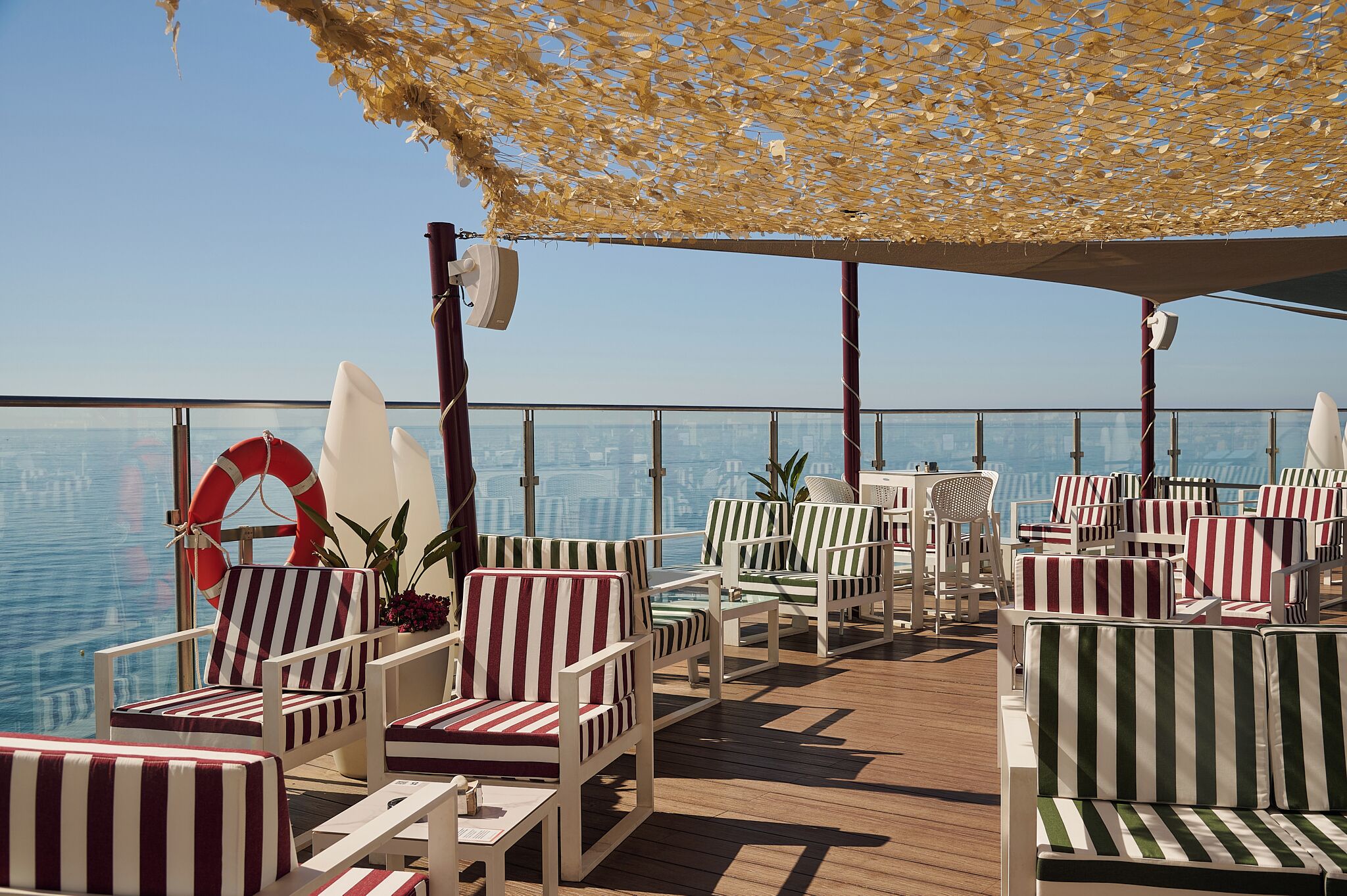 A deck with striped chairs and tables, a lifebuoy, and a view of the water.