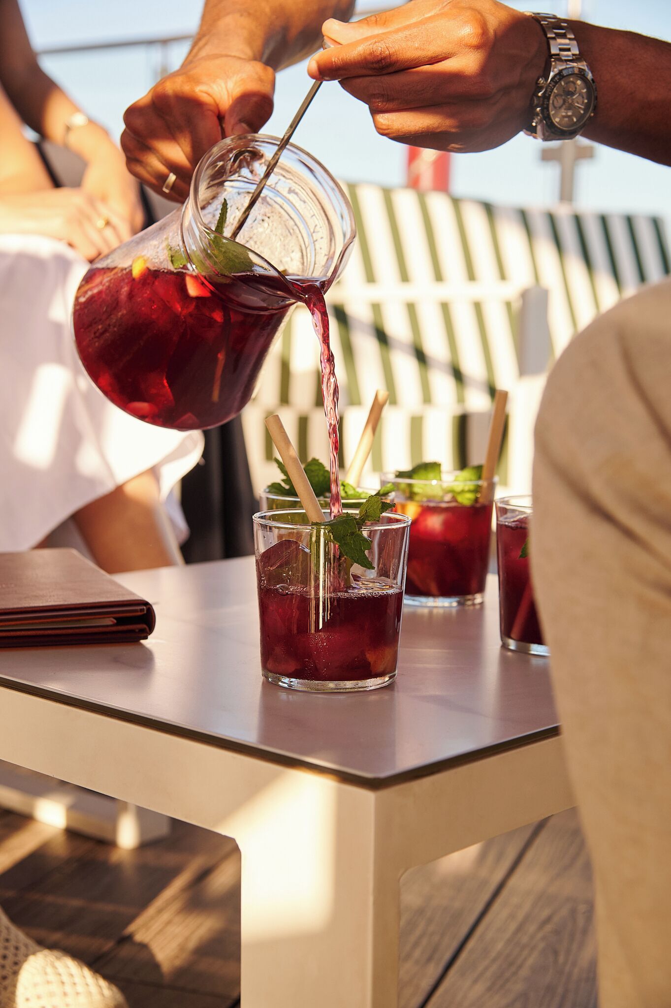 A person pouring a drink into a glass with a straw and mint garnish.