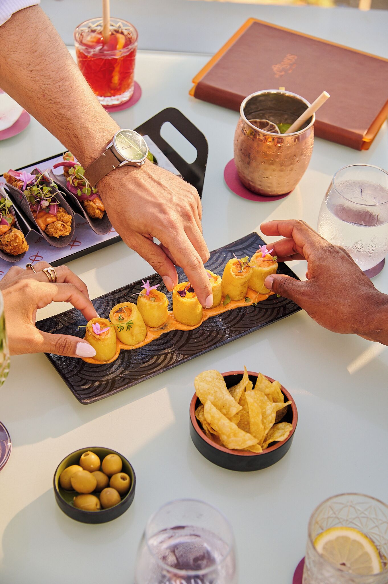 A table with a plate of appetizers, a drink, and a menu.