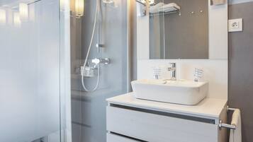 A modern bathroom with a glass shower enclosure, a white vanity with a large mirror, and a dark wood floor.