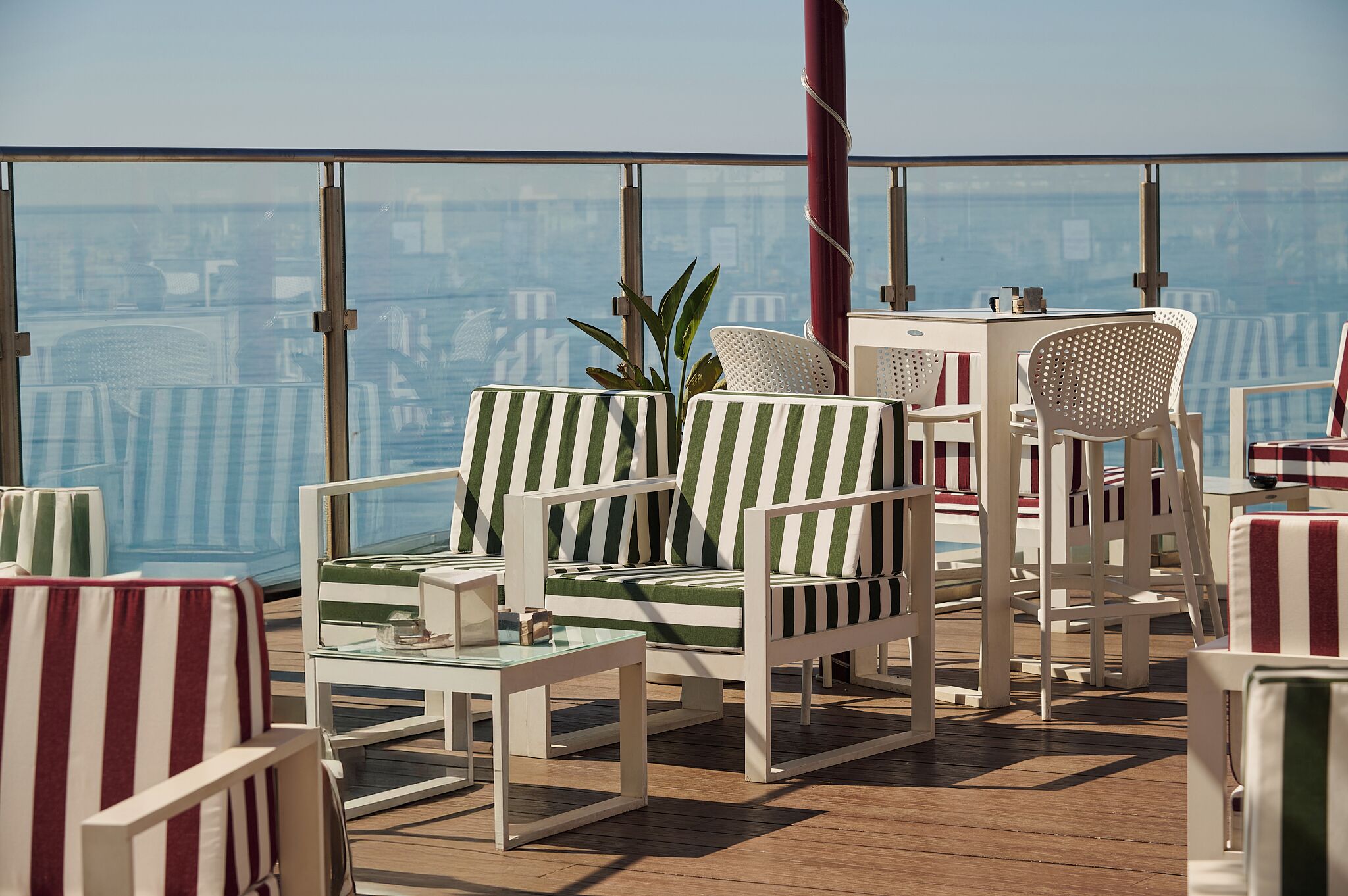 Eine Dachterrasse mit gestreiften Liegestühlen, einem Glastisch und Blick auf die Stadt.