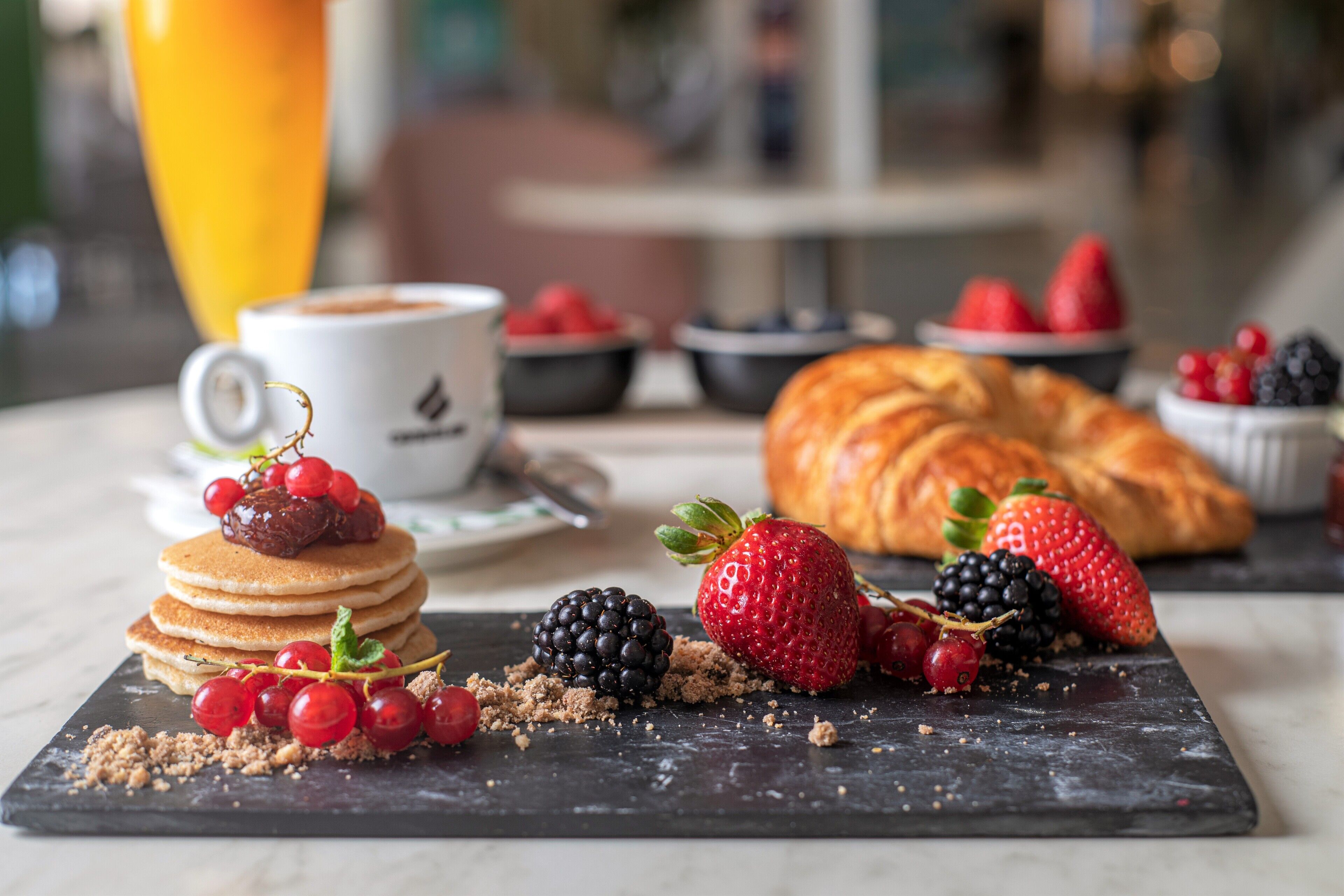 Un esmorzar amb crepes, maduixes, nabarrets i un croissant sobre una taula de pissarra.