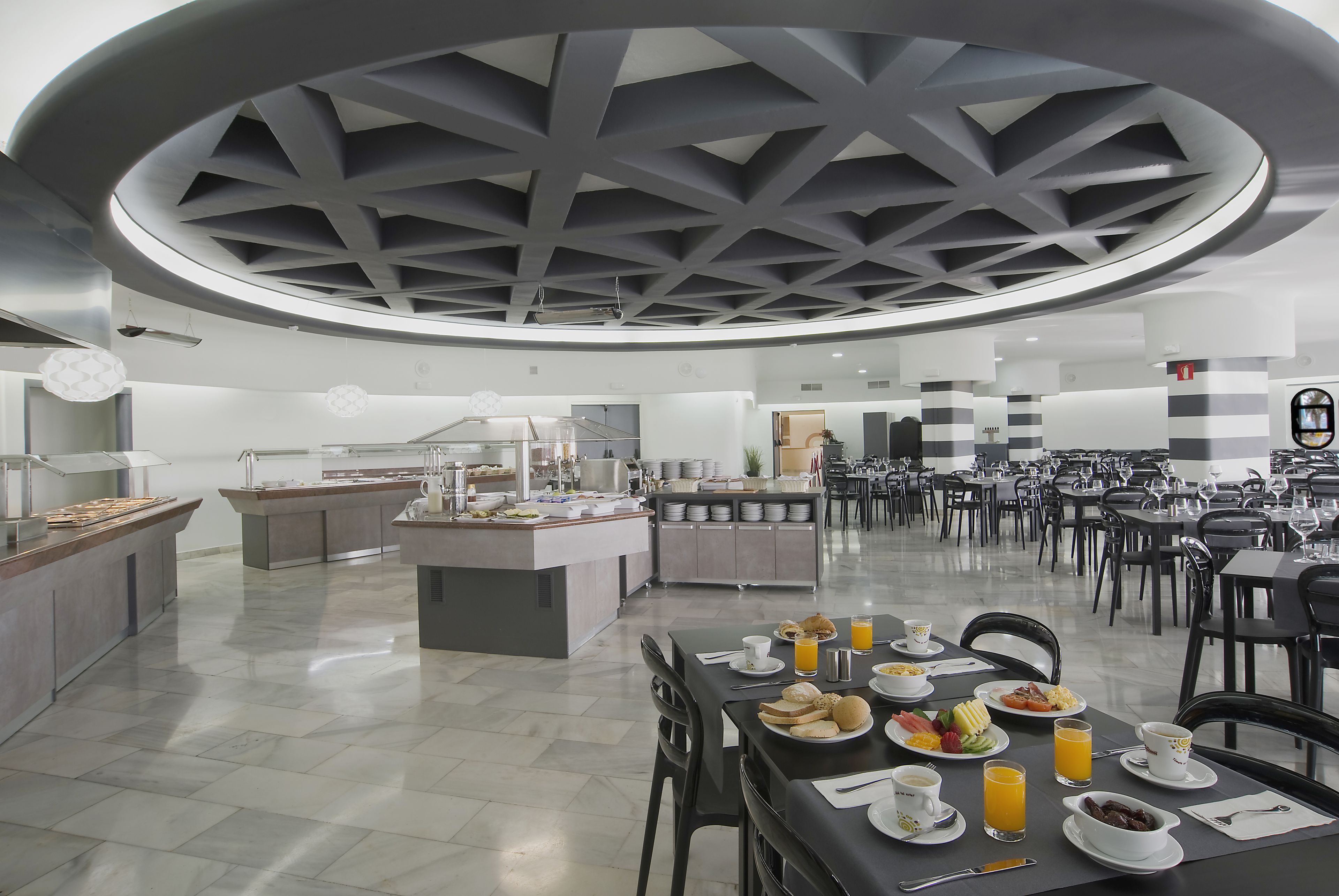 A modern dining area with a central island, multiple tables, and a unique ceiling design.