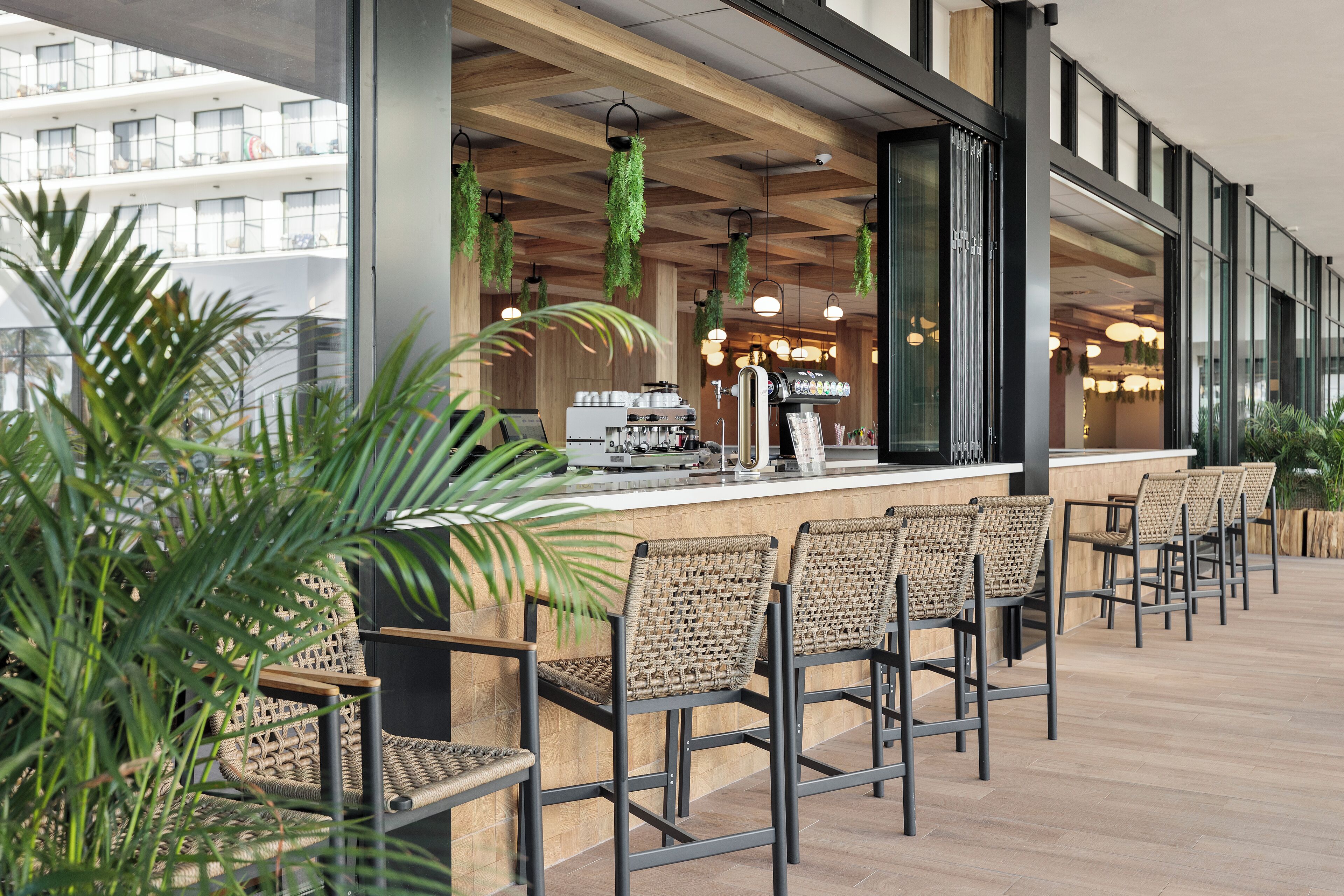 A modern bar area with wicker chairs, a coffee machine, and hanging greenery.