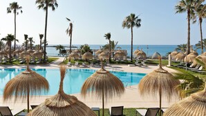 A poolside area with thatched umbrellas, palm trees, and lounge chairs. - Hotel Best Tritón (Benalmádena)