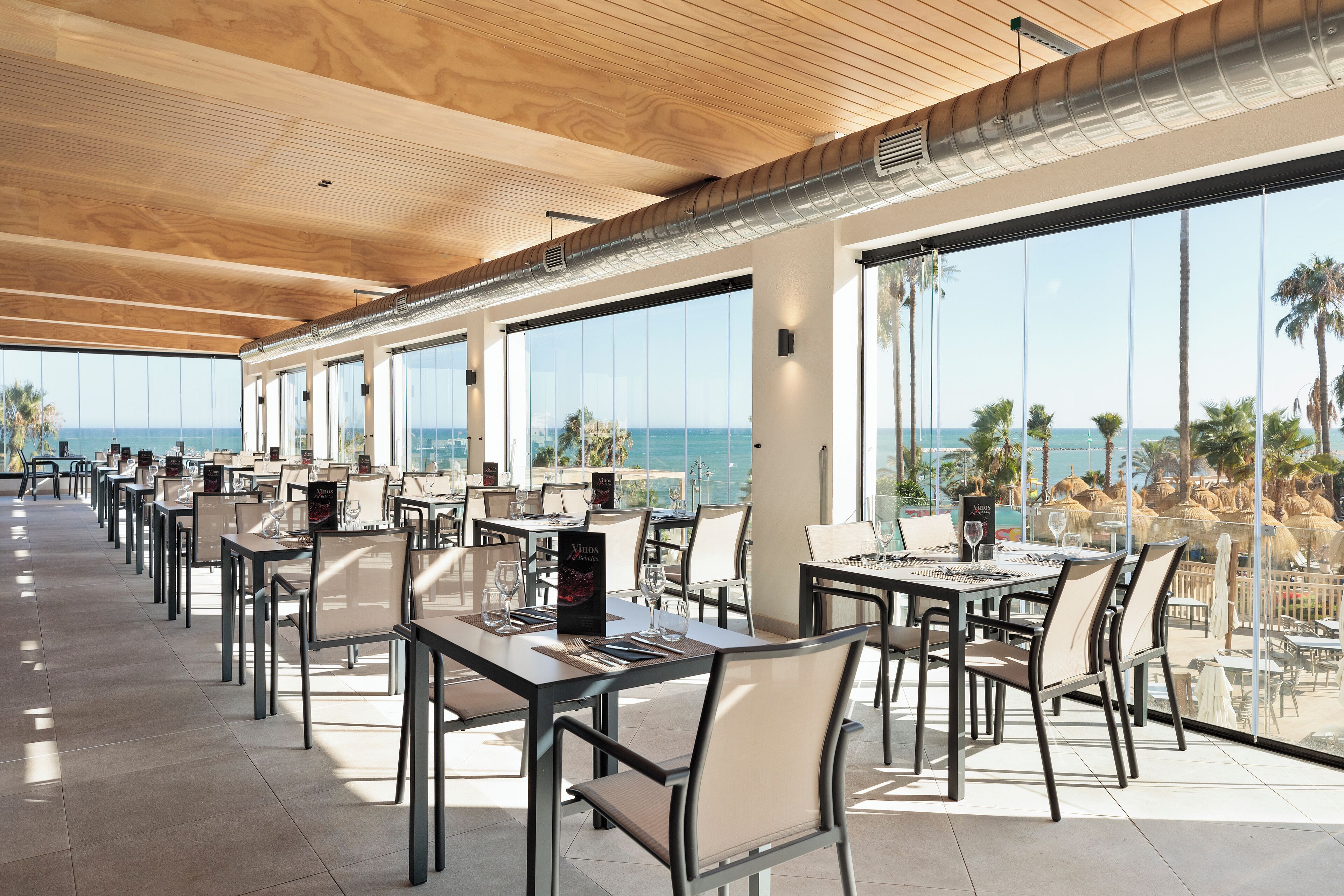 A restaurant with a long table layout, large windows, and a view of the ocean.