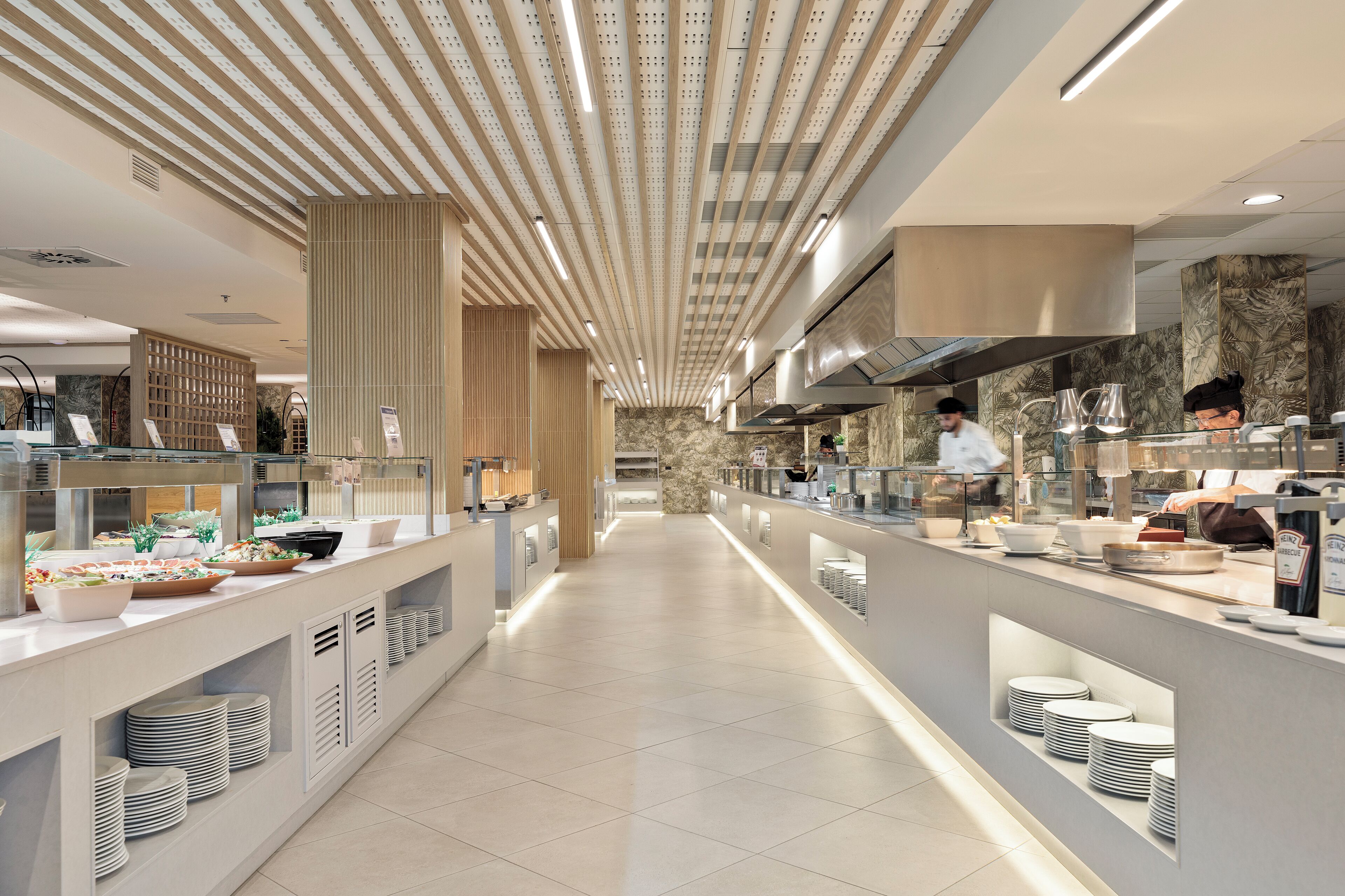 A modern kitchen with a long counter, stainless steel appliances, and a chef preparing food.