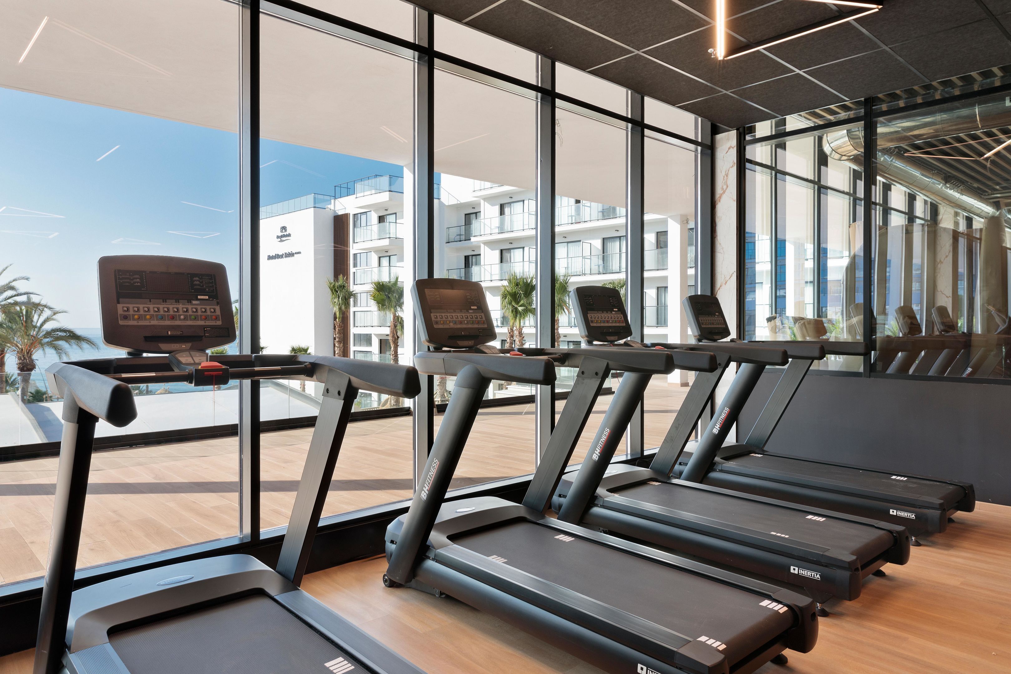 A gym with treadmills, exercise equipment, and large windows offering views of the outside.