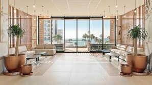 A modern hotel lobby with a large seating area, two large potted plants, and a view of the beach and ocean through floor-to-ceiling glass doors. - Hotel Best Tritón (Benalmádena)